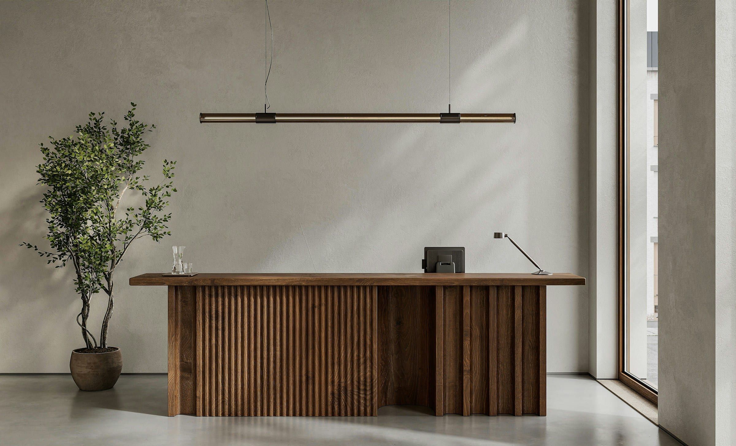 Office reception desk against a grey wall, with a tree and window light