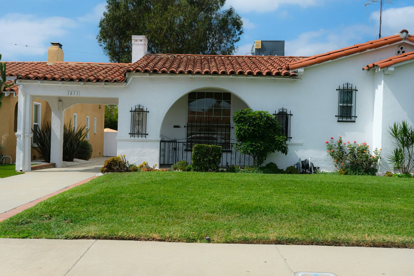Front of a white stucco Spanish-style house with a red tile roof, arched porch and green lawn