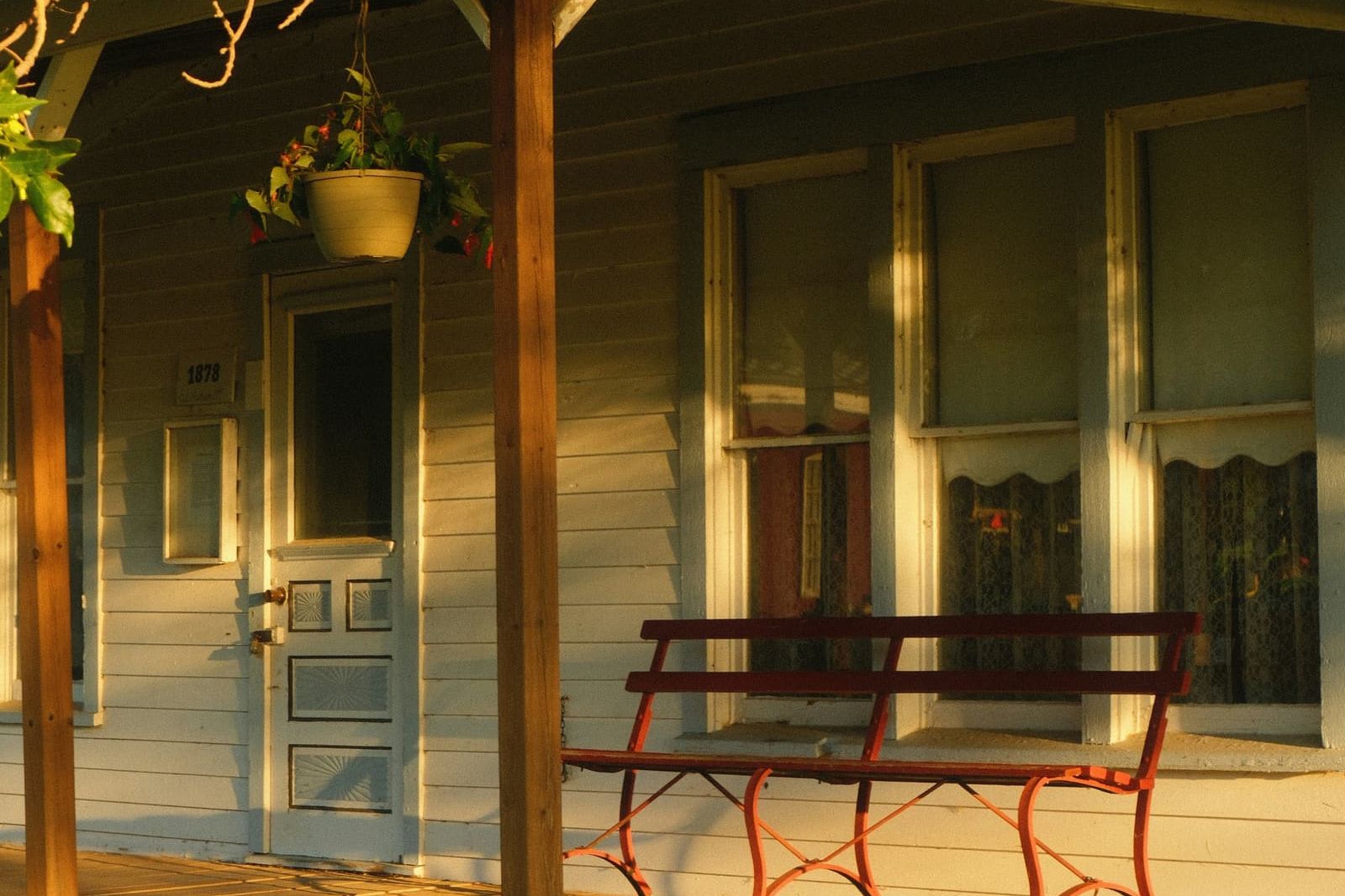 Sunlit wooden porch of a pale green clapboard house with cream trim and a red bench