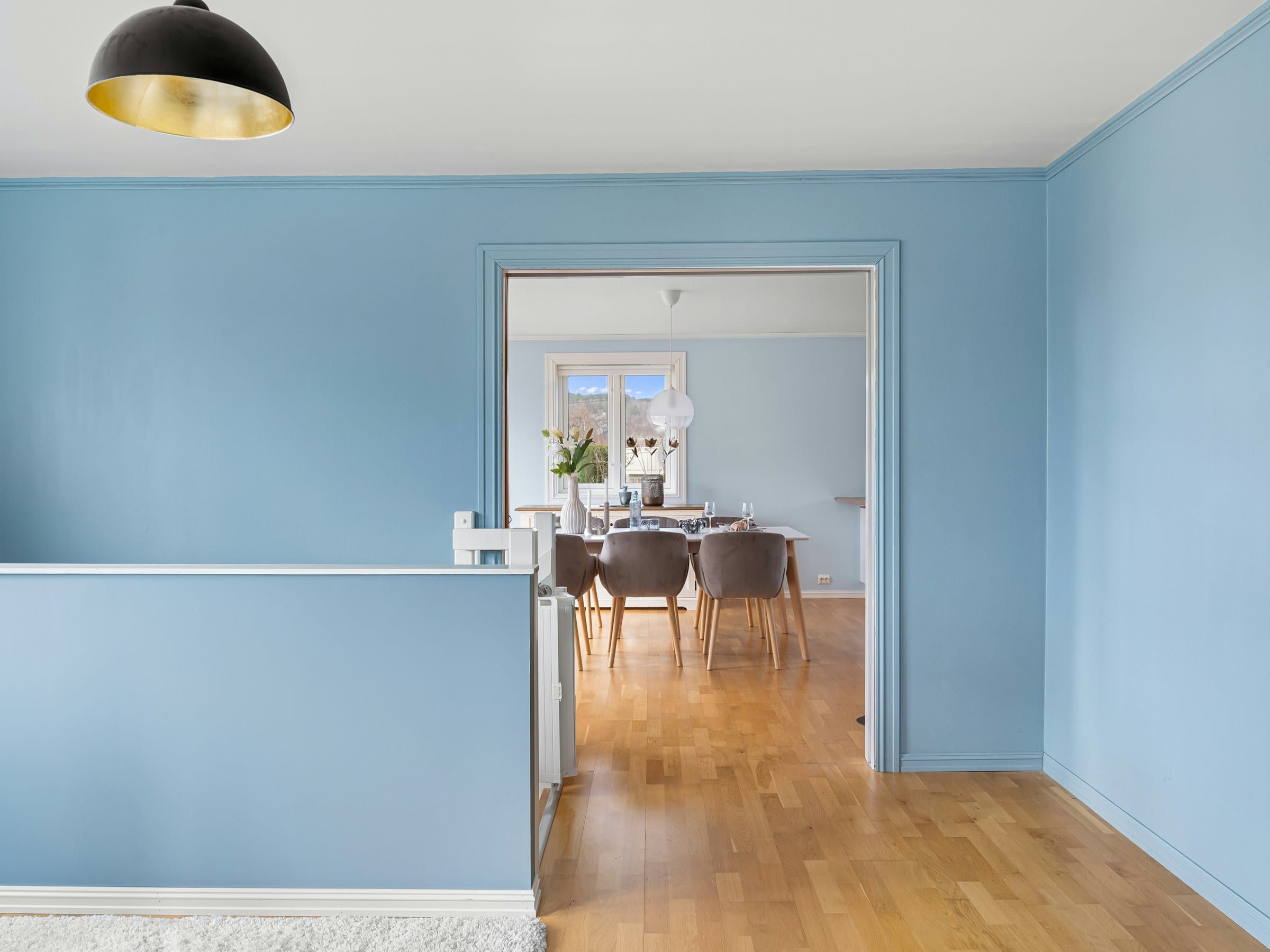 Small treatment or consulting room with pale blue walls, white trim and a window, freshly painted and empty