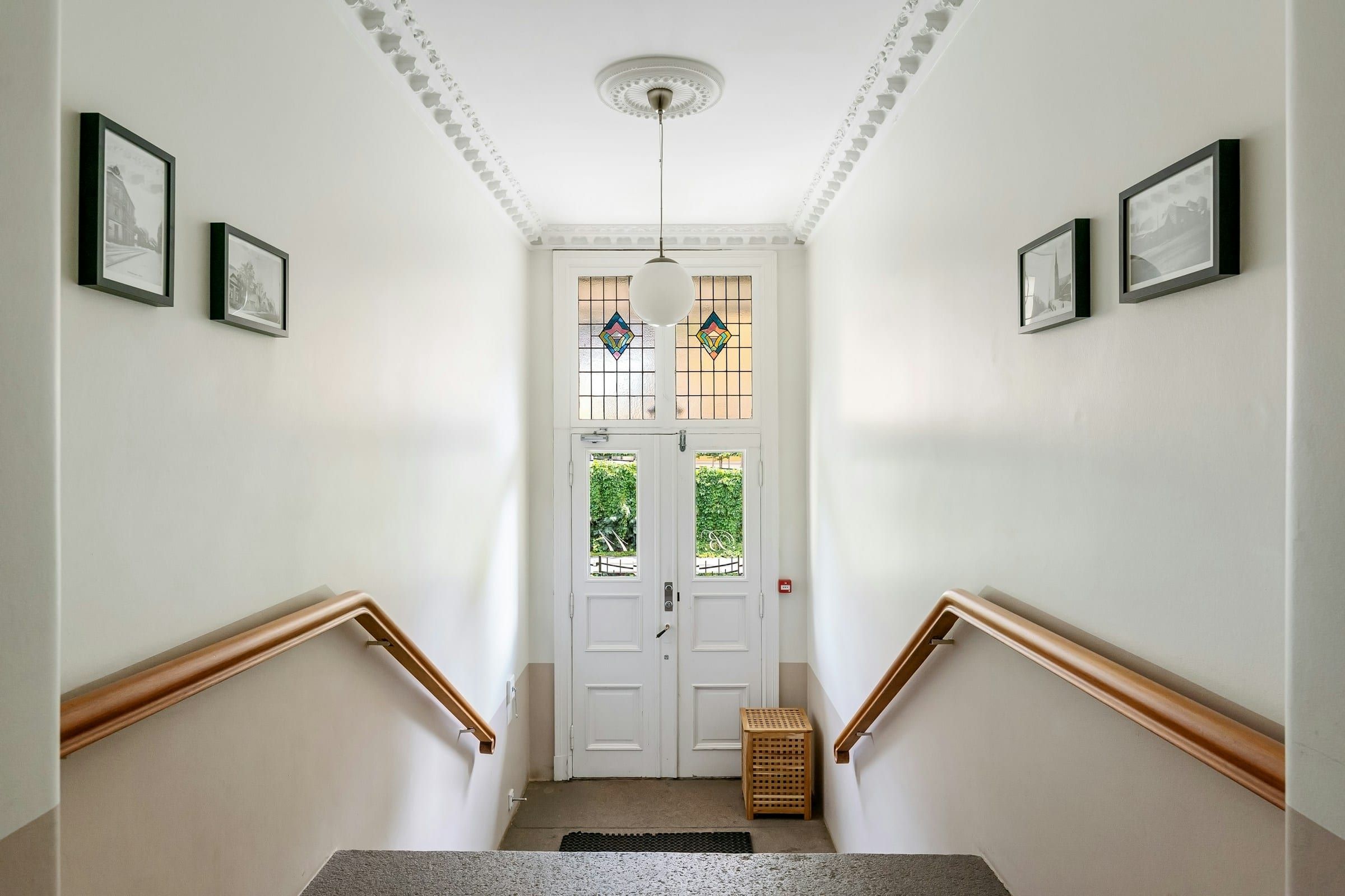 White stairwell hall with wooden handrails, framed pictures and a white front door