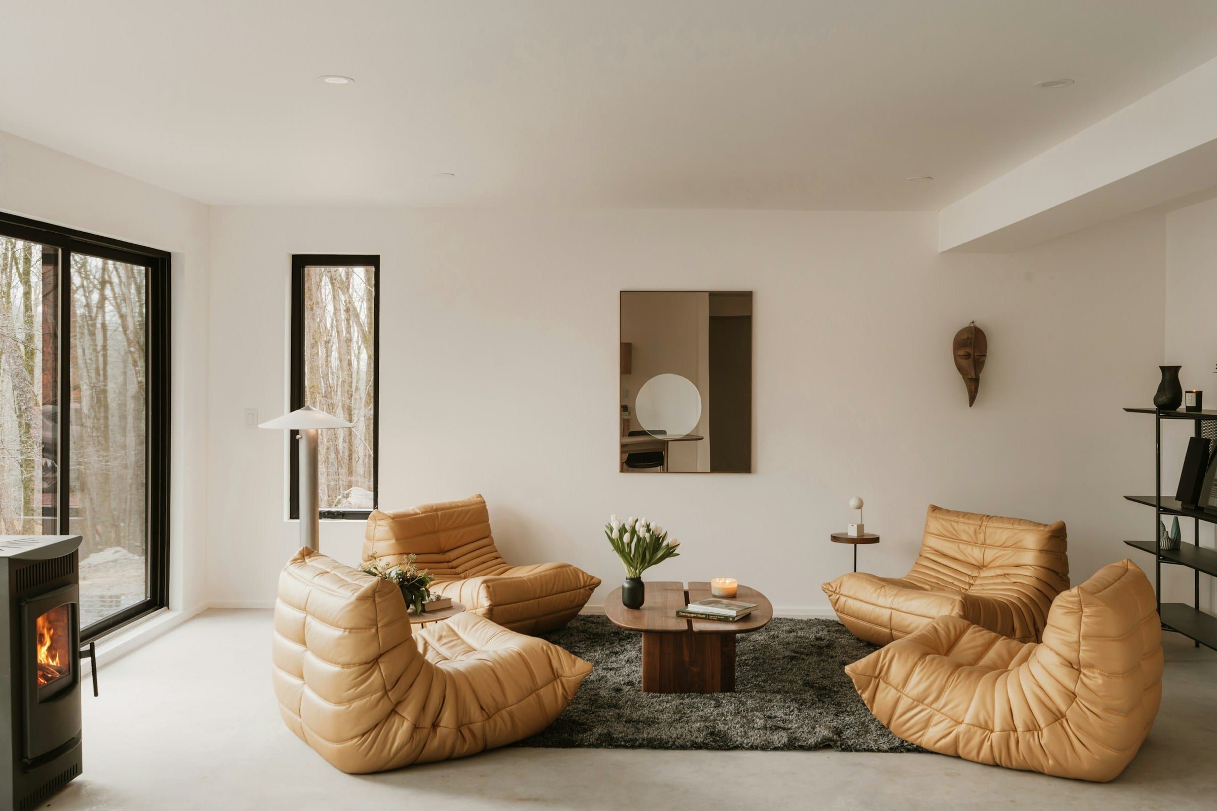 Bungalow living room with white walls, a warm wood floor, a black window frame and a wood stove