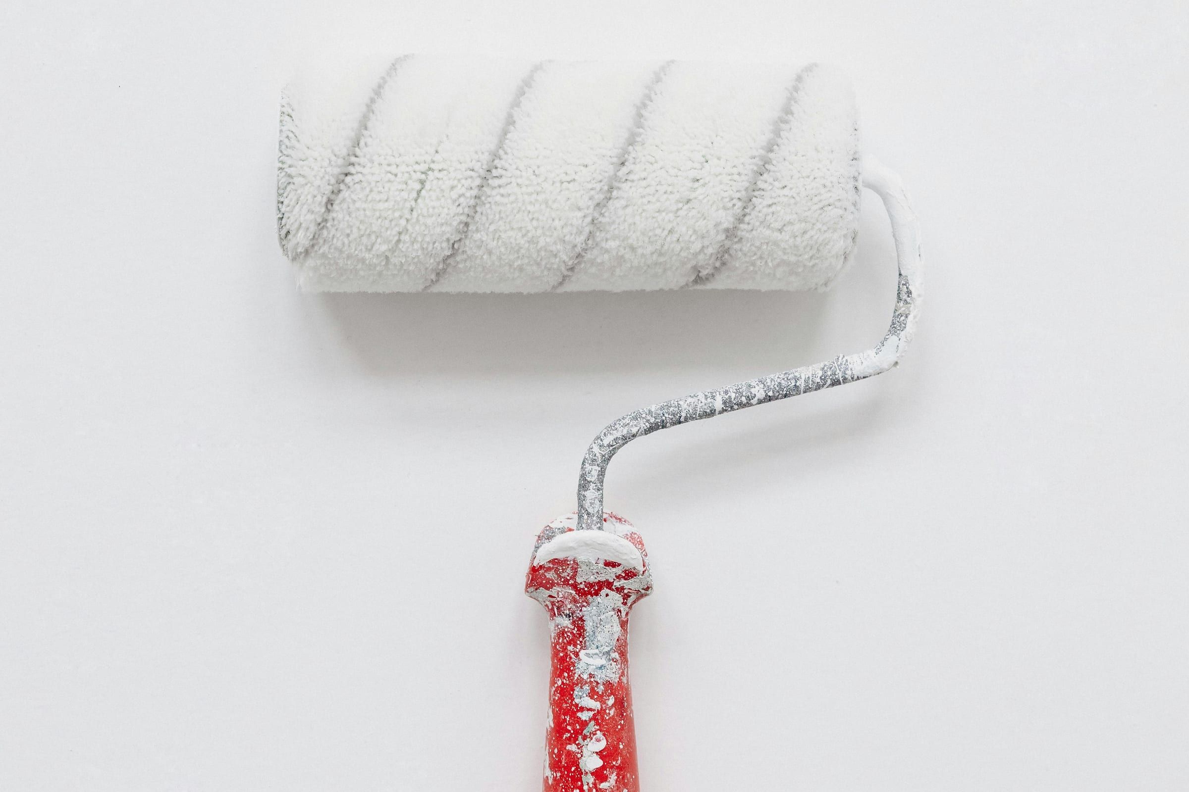 White paint roller with a red handle lying on a white wall